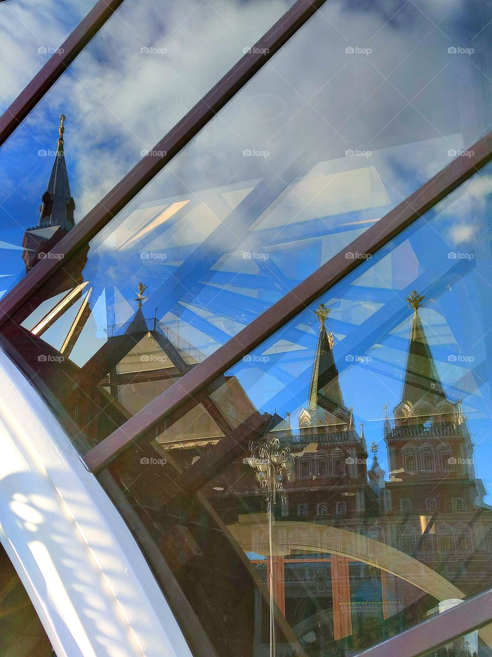 Reflection in the showcase: domes of the towers of the Resurrection Gate, blue sky with white clouds. The Red Square.  Moscow