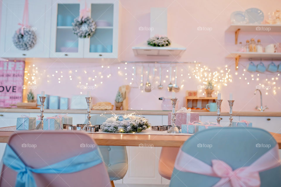 Festive winter cozy kitchen interior with garlands, decorations and gifts.  Christmas dinner at the decorated table.