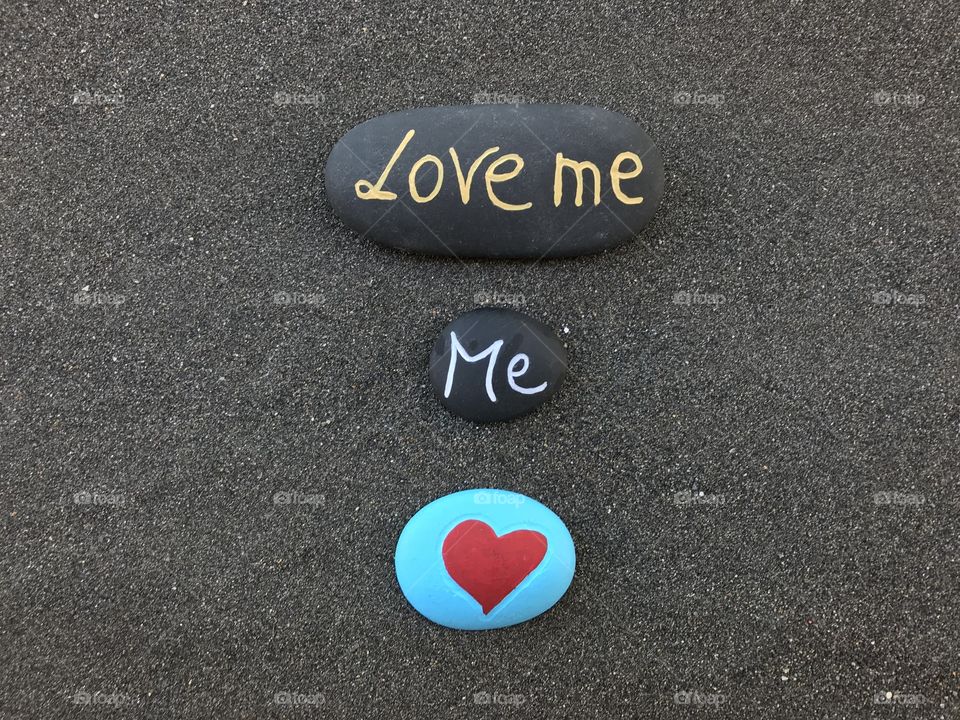 Love me message carved on colored stones over black volcanic sand