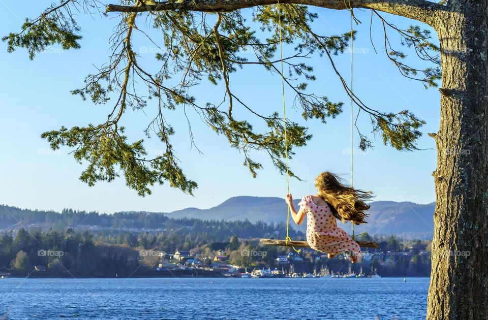 Girl with long hair blowing in the wind is swinging on rope swing in a scenic ocean setting