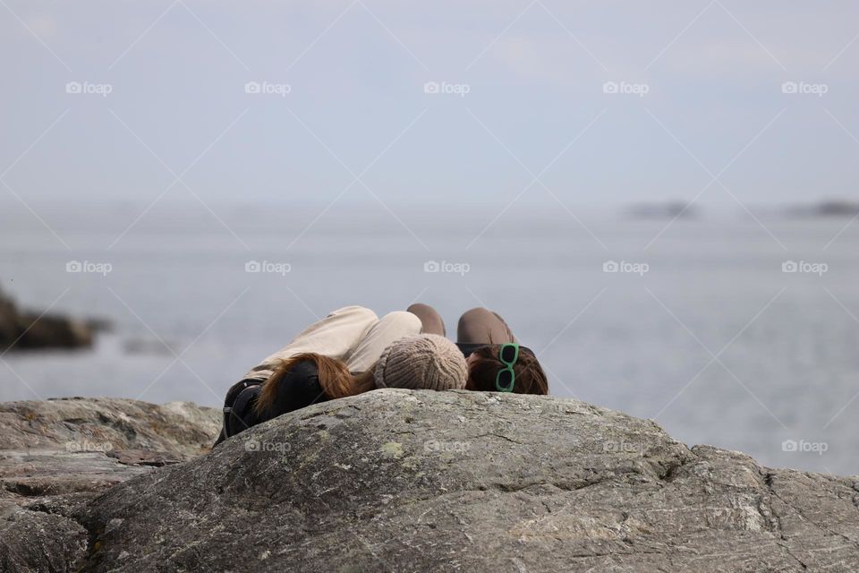 Friends laying on a rock by the shore 