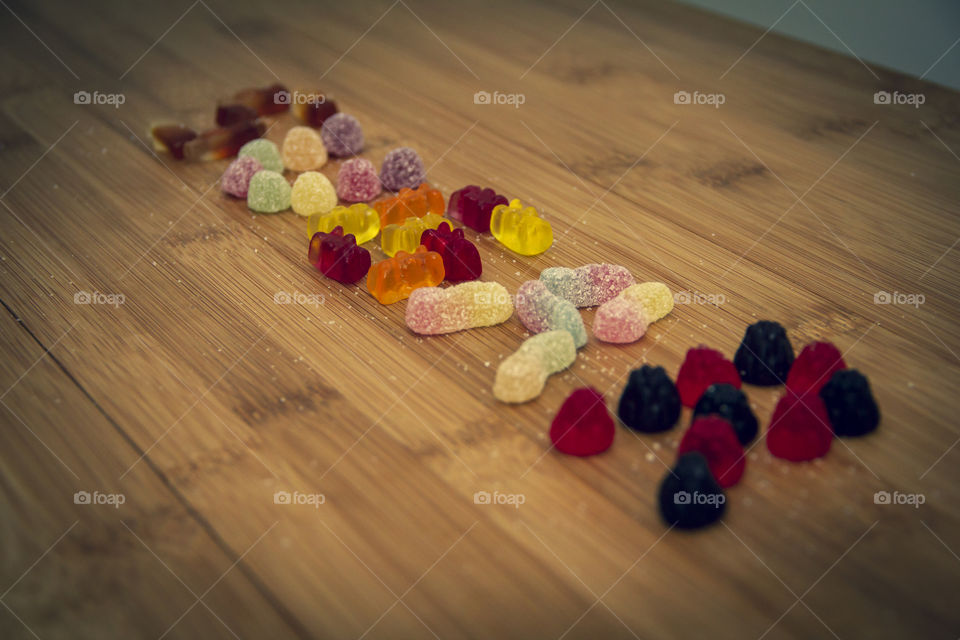 The word sugar spelled out on a wooden table with different kinds of colorful candy.