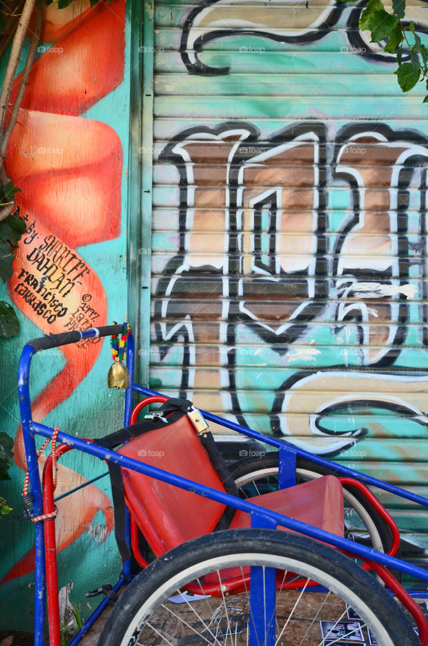 Detail of a rickshaw parked in front of a mural in the Mission district of San Francisco, California 