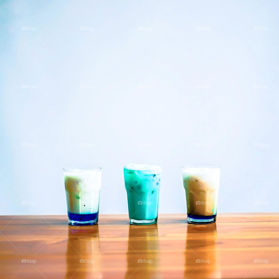 Three glasses of drink are lined up on a wooden table. Drink. Beverages. Glass. Table. Wood. Wooden table. Café. Cold. Ice. Fluid. Liquid. Photography. Aesthetic. Isolated background. Tranquil. Scene