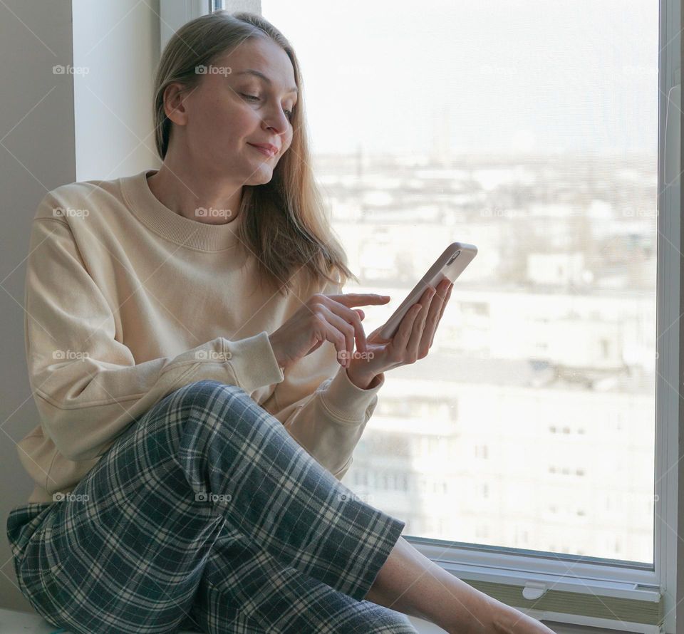 A woman sitting by the window and using a smartphone 