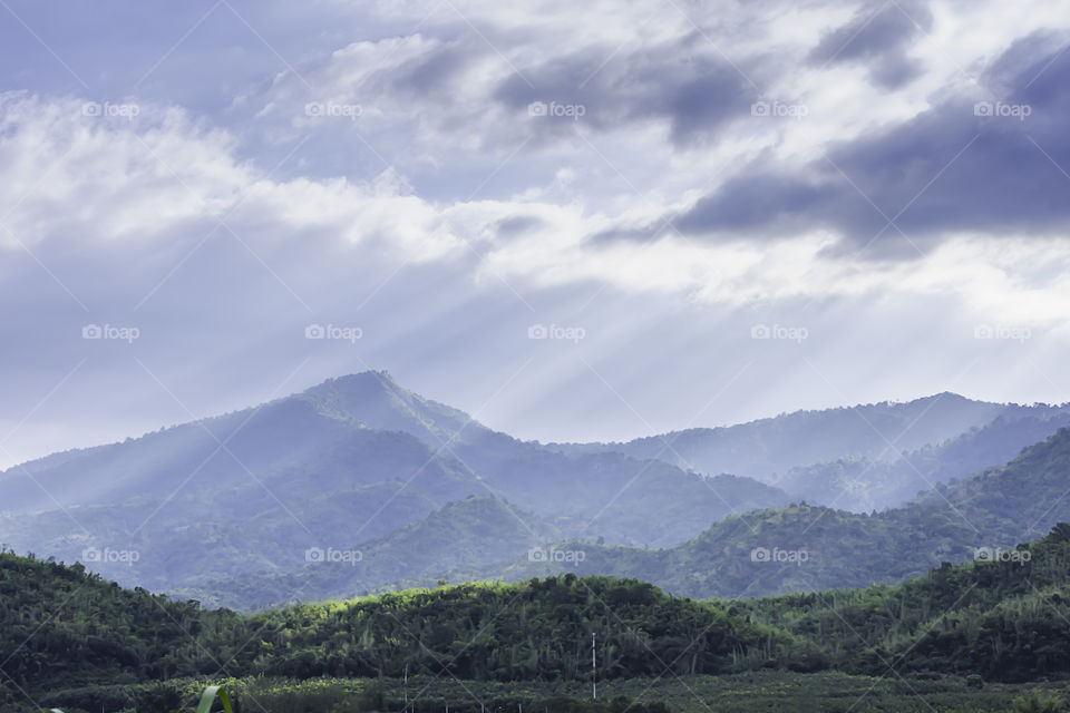 The sun shining through the clouds to the trees on the mountain at Suan phueng of Ratchaburi in Thailand.