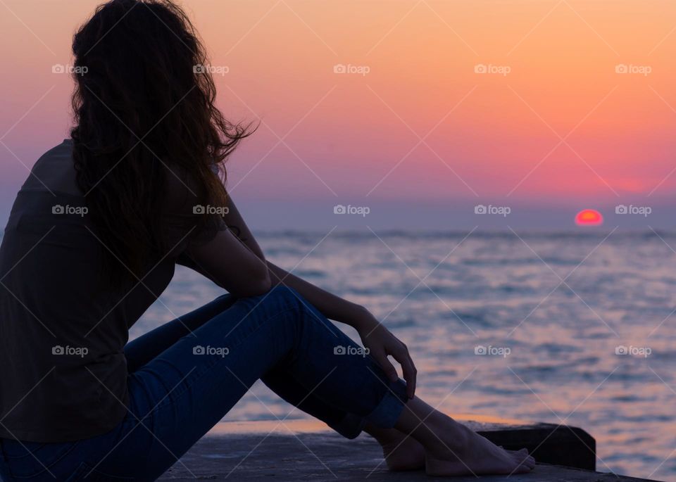silhouette figure of a woman sitting on a dock taking in the beautiful orange and pink sunset over the sparkling blue water and the the stillness within