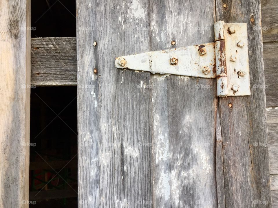 Rusty hinge with peeling white paint on a weathered wooden door 
