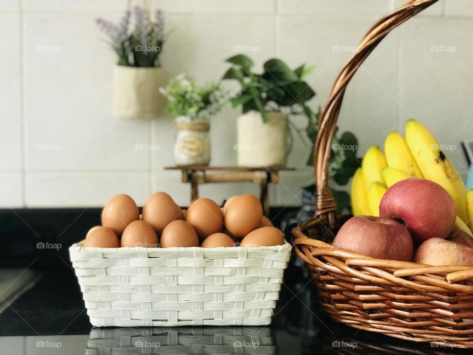 A basket full of fruits and eggs on kitchen cabinet 