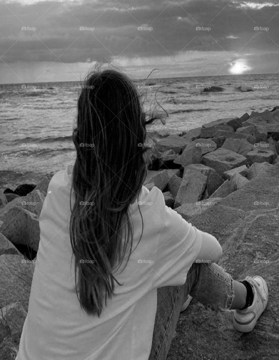 A dreamy and absorbed girl who lives romance and love and plays in a scene that draws attention with the setting sun and the reflection of sunset rays on the waves of sea water with the appearance of a captivating sunset light.