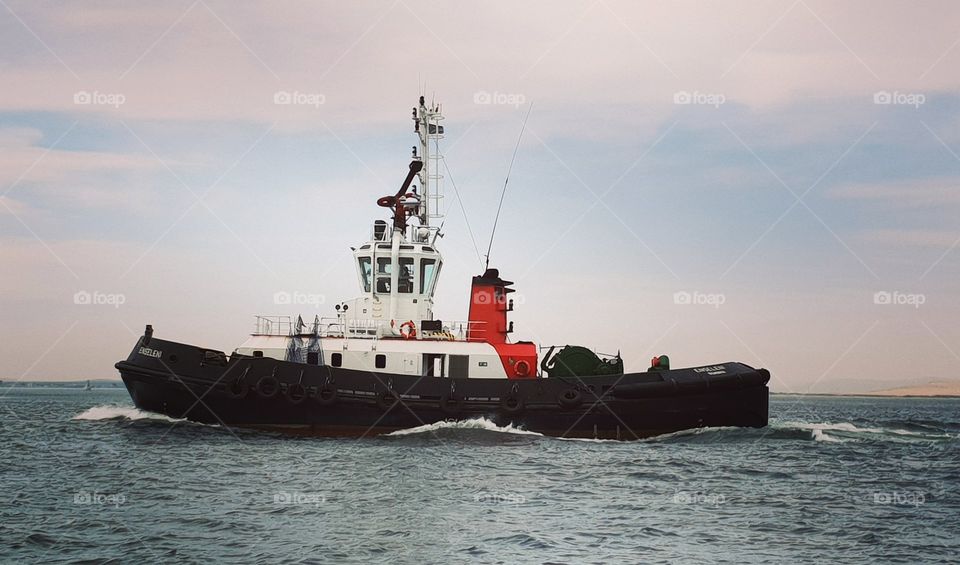 A tugboat moving across a calm ocean. A beautiful backdrop of pastel clouds in the background.
