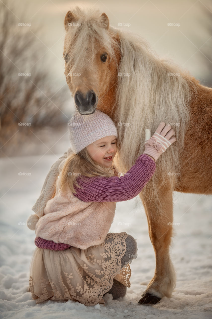 Little girl with palomino pony at winter sunny day