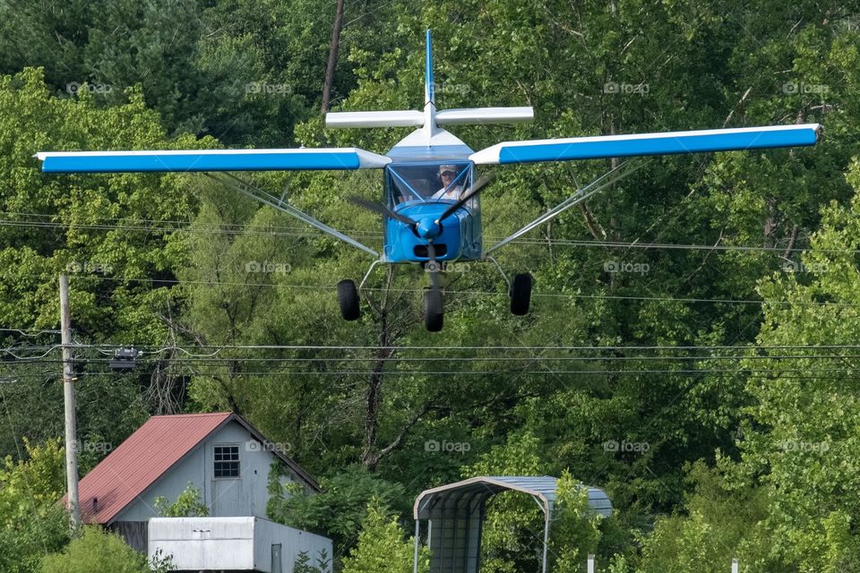 Foap, A to B: A pilot comes in for a landing, which requires clearing the tree line, then the power lines, then the fence to land safely in the grassy runway in the pasture as long as the cows are out of the way.