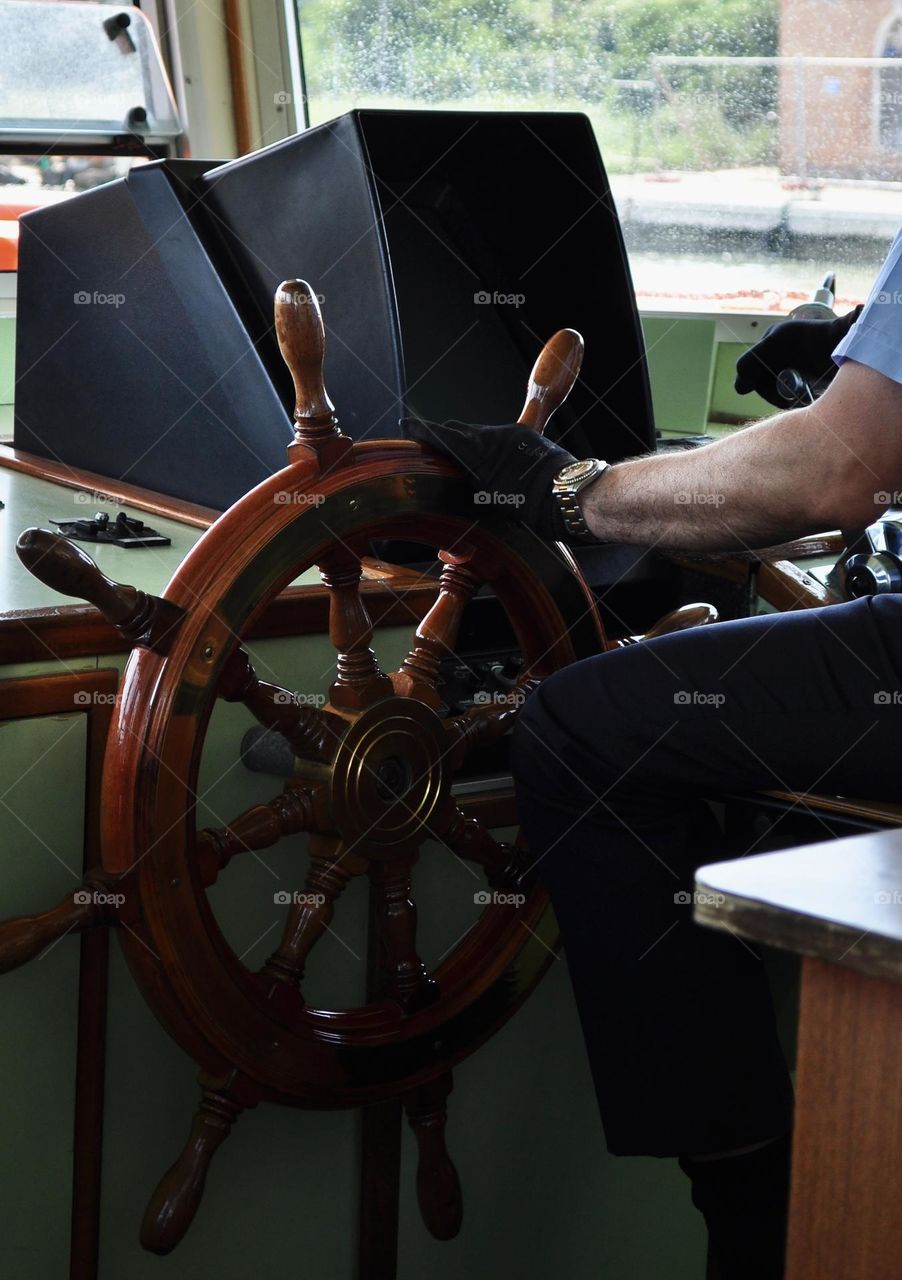 Large wooden nautical helm wheel being driven by human hands 