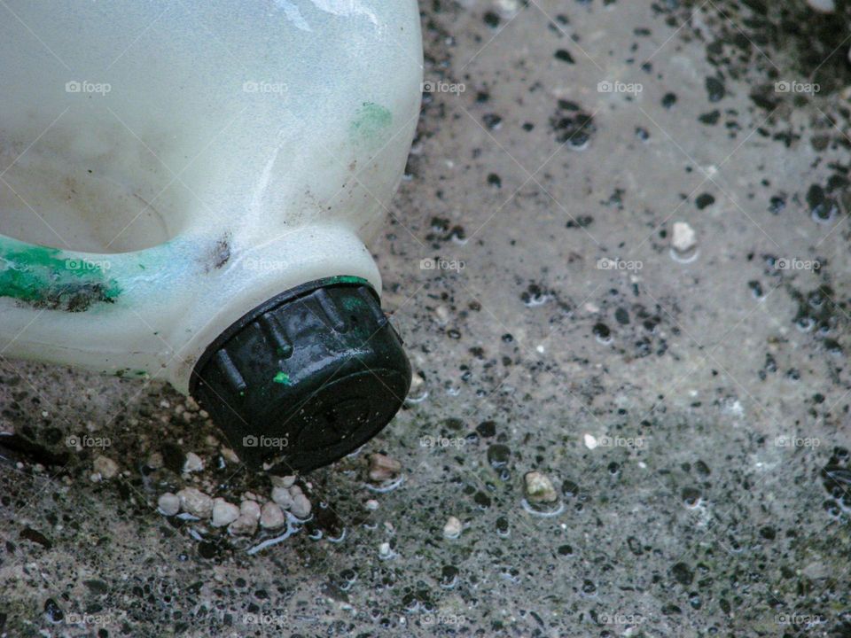 Close-up view of a white plastic bottle with a black cap lying on the muddy ground in high angle view