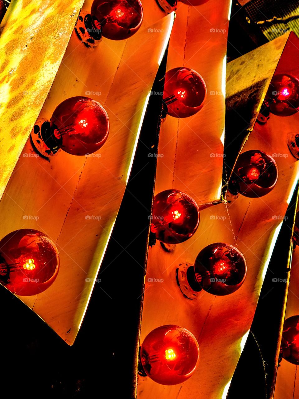 Part of a lighted metal sign of the letter M with colored lights illuminating in the night with the colors of reds, oranges, and yellows