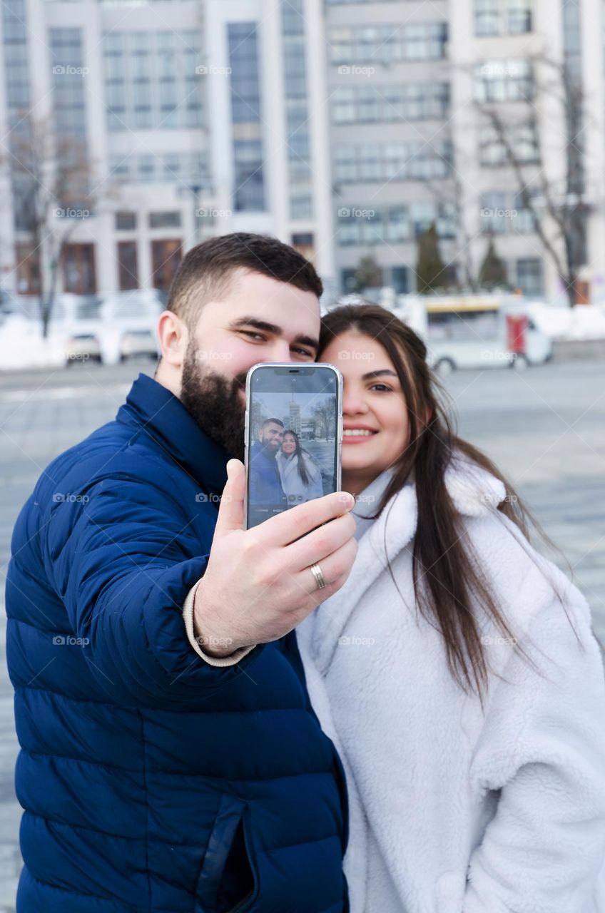 Portrait of young happy couple, bearded man and brunette woman woman relaxing in winter city. Laptop. Phone. Technology. Selfie. Social media. Video call