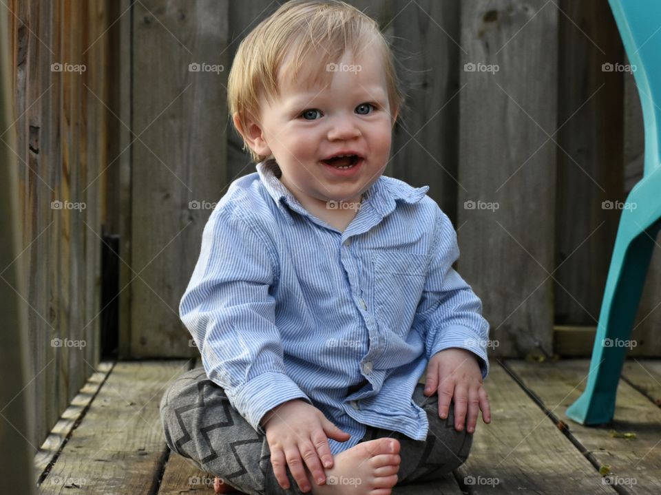 Cute happy barefoot baby boy playing on wooden porch 