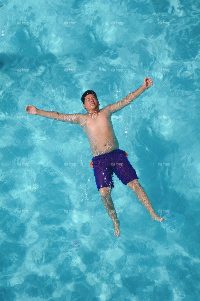 A man floats on his back in a cool blue refreshing swimming pool. 
