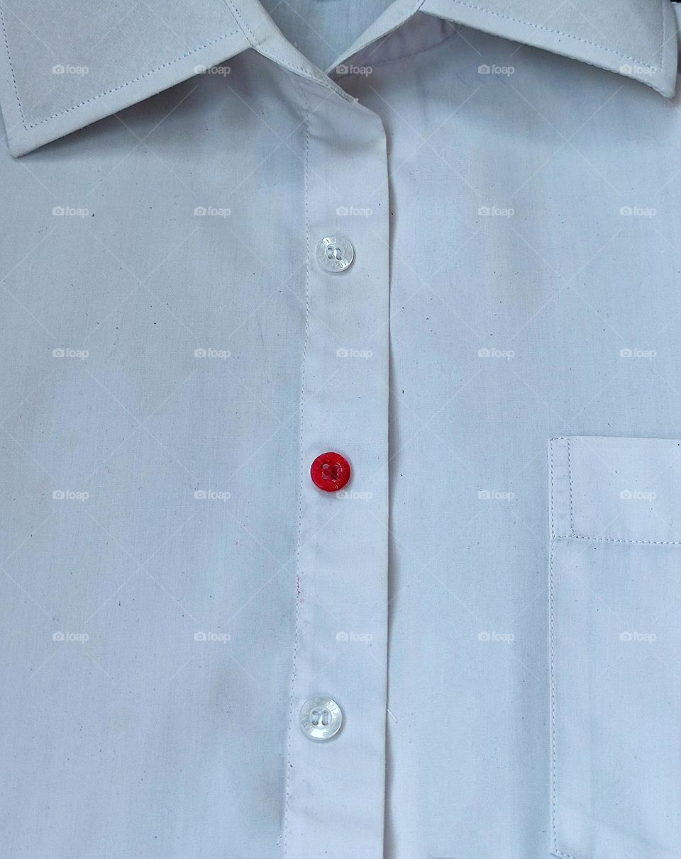 Minimalism of the object.  White shirt.  The shirt has a row of transparent buttons, including a bright red button.  Minimalism in contrast