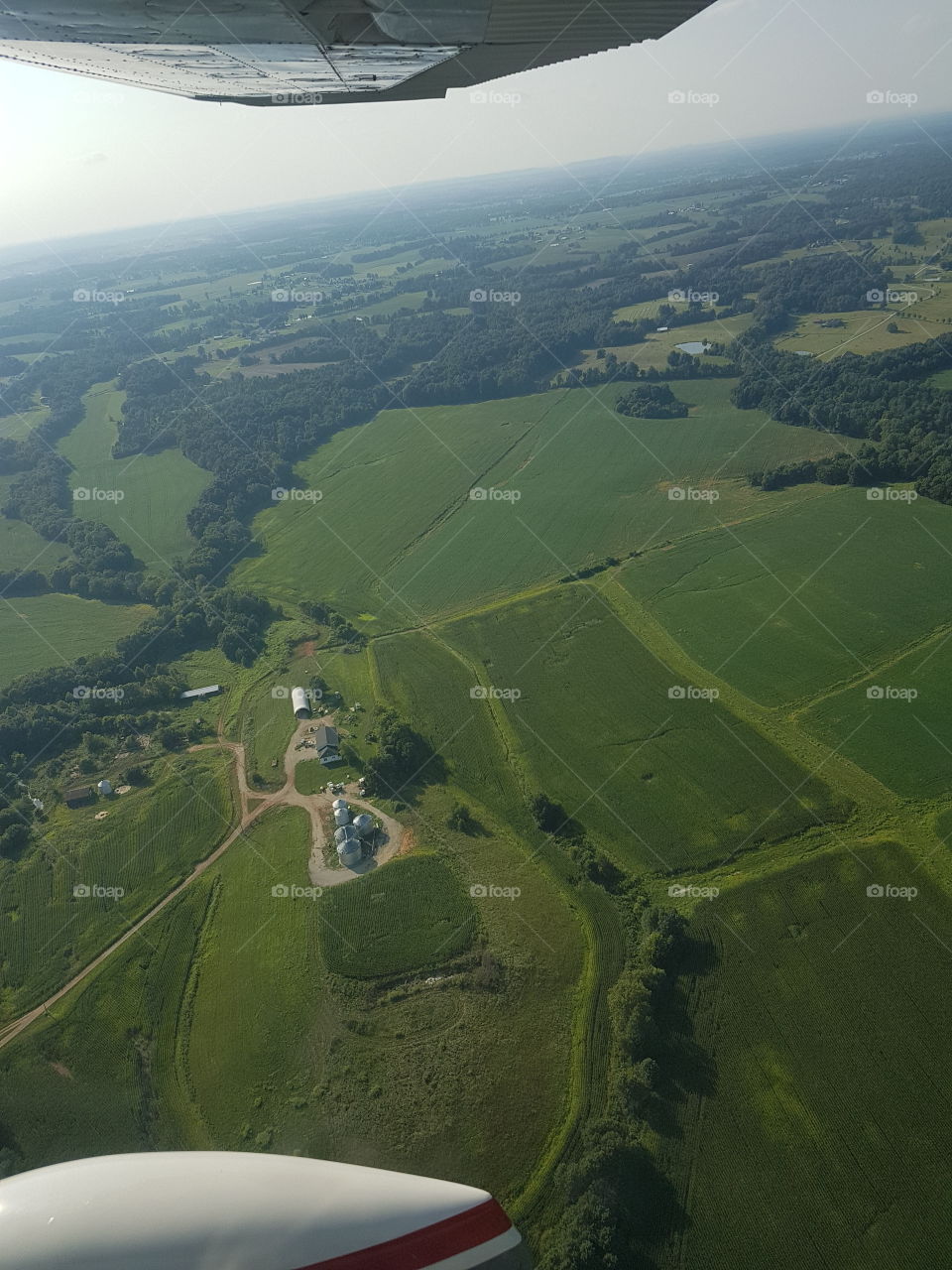Gorgeous aerial view of cultivated  farmland, barn and silos in Summer with forested boundaries