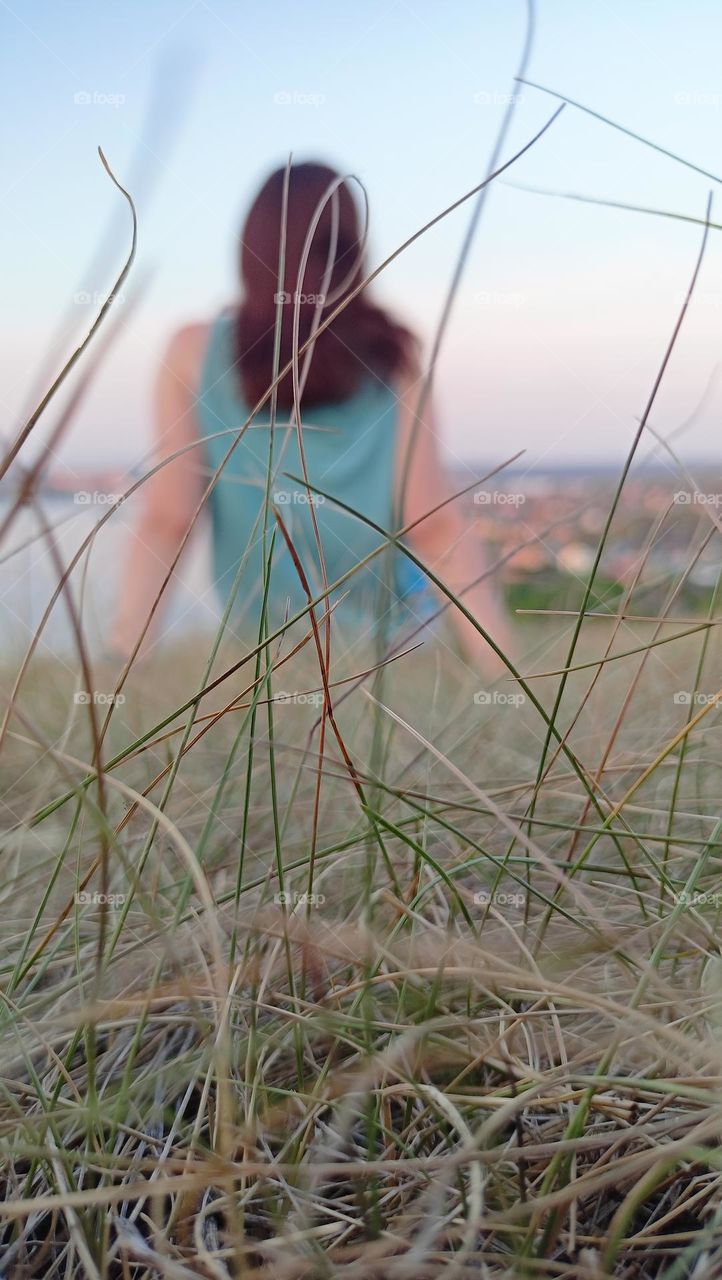 girl looks into the distance, meditation, contemplation nature, view from the mountain to the city, pond, water, summer, evening, calmness, peace, light breeze, the girl is sitting on the grass