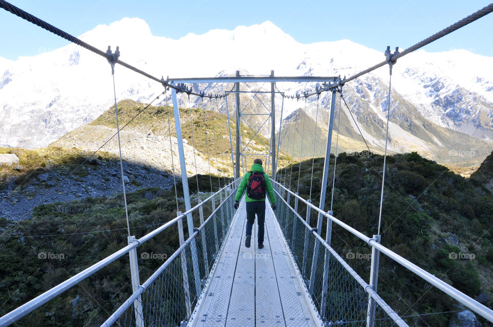 man walking over a bridge in snowy mountains