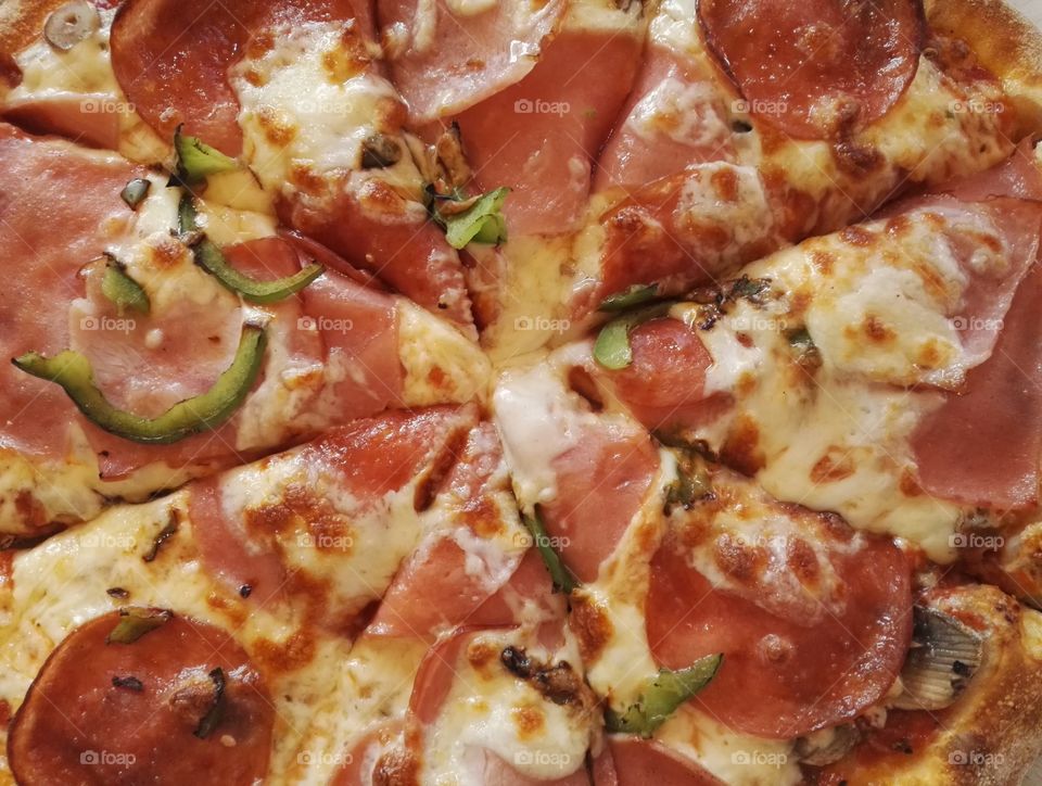 cut pizza with ham, bacon, salami, fresh mushrooms and green pepper from wood fired oven closeup