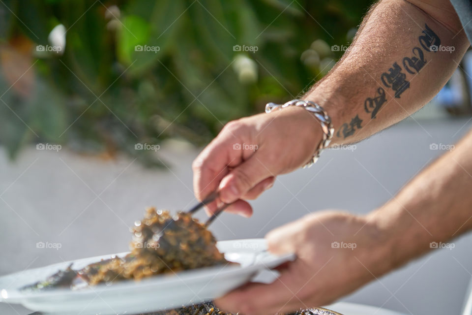 Brazo tatuado sirviendo un plato de Arroz Negro. 