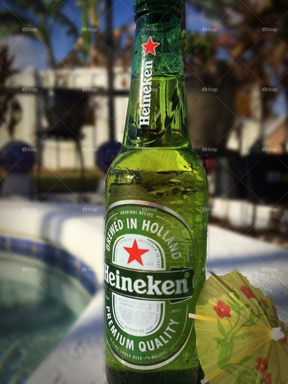 Heineken bottle of beer with mini umbrella by the pool