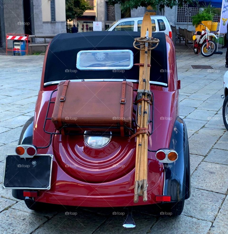 Fiat 500 Topolino 1938. Italian car in burgundy color. An old suitcase and skis are attached to the back of the car