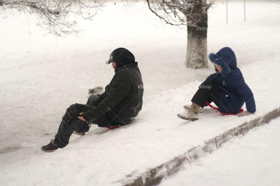 Dad and daughter ride a hill in winter