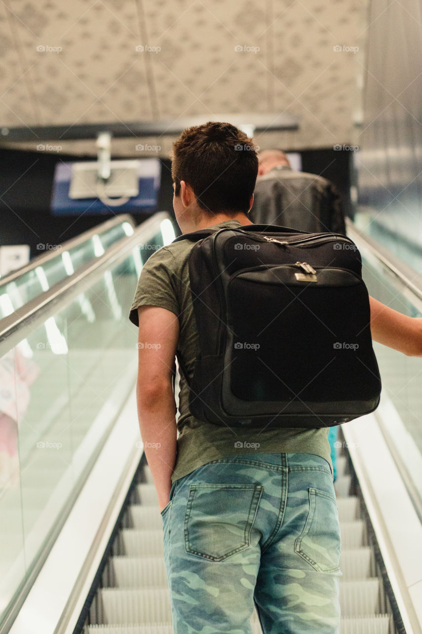 Young man standing on a escalator in the railway station, travelling with backpack