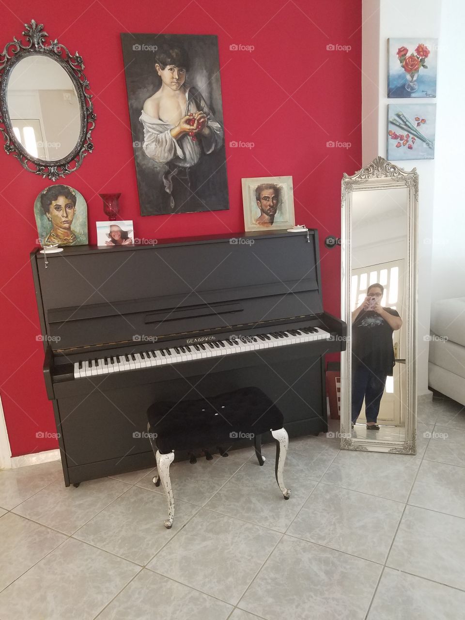 A black piano with several pieces of art depicted on a red wall. The floor is made of marble.