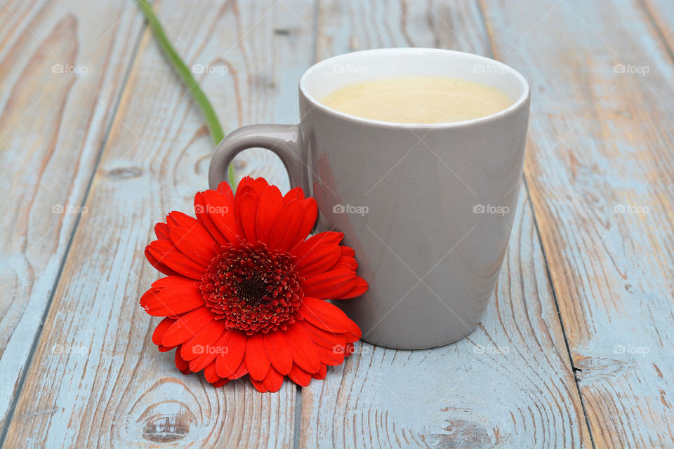 cup of coffee on a wooden background with red daisy flower decoration