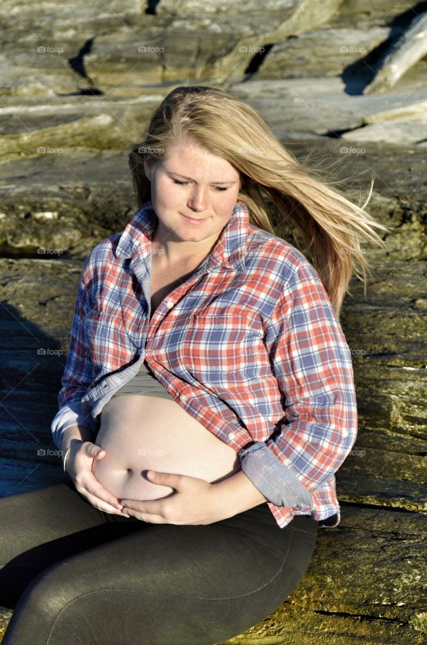 Smiling pregnant woman sitting on rock
