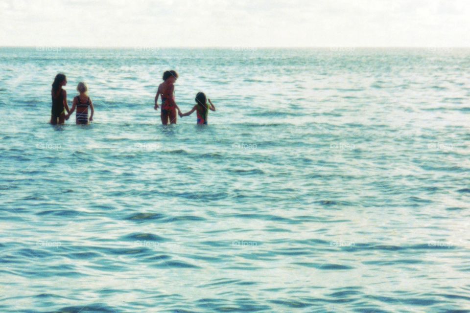 Children walking hand in hand into the ocean