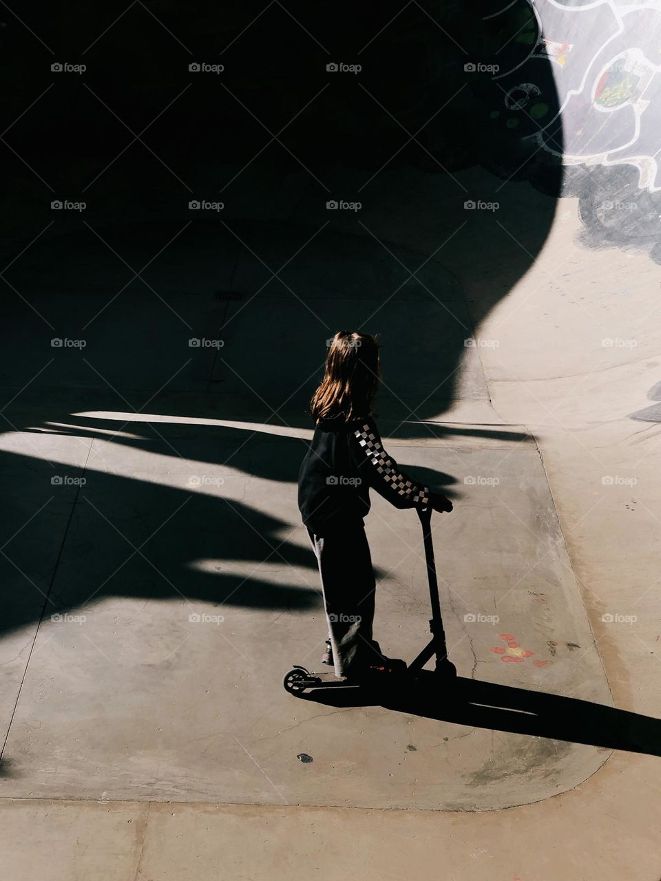 Little brunette girl with scooter in sunny day