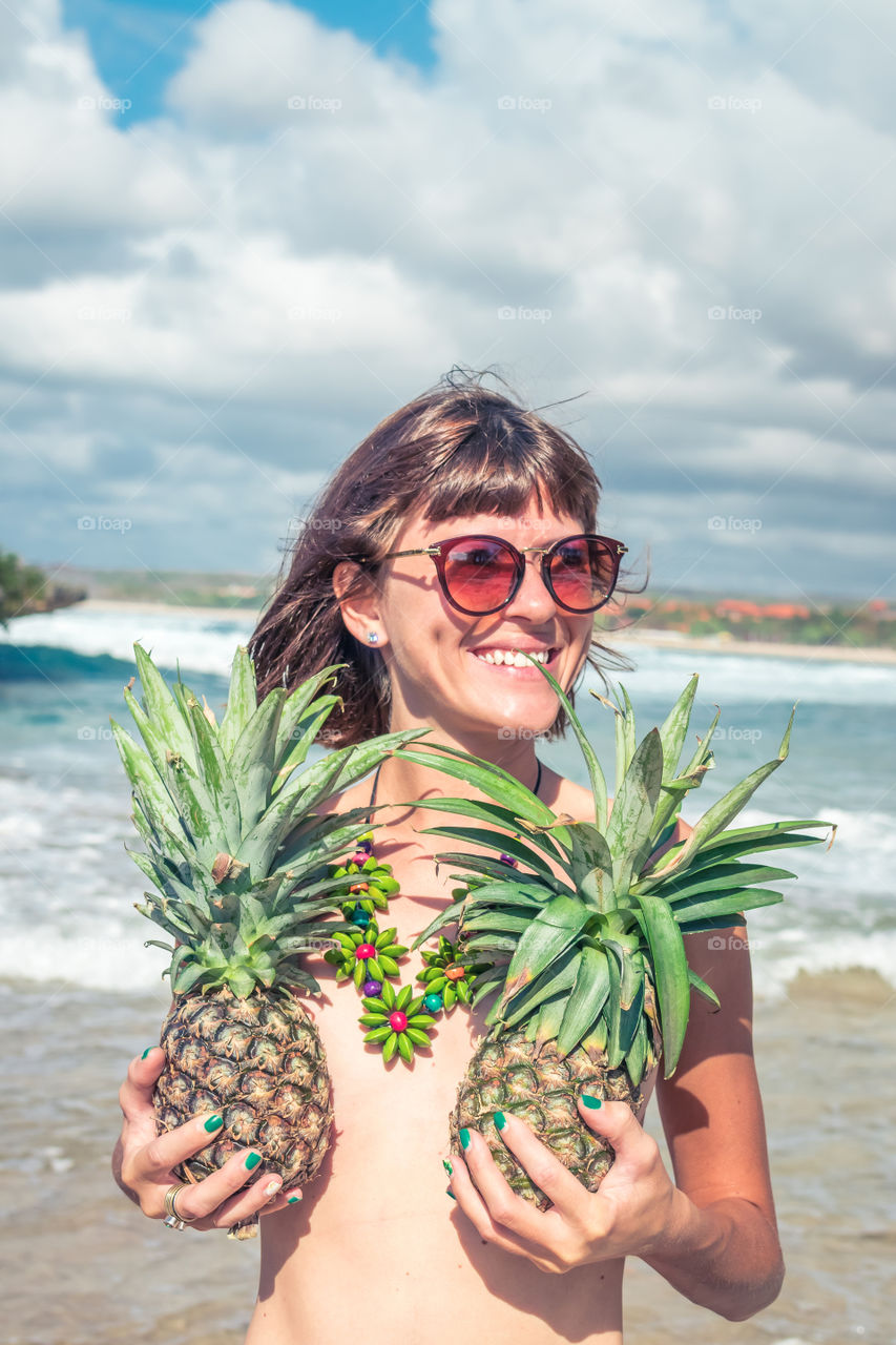 The girl is photographed on the beach with pineapples. Bali island.