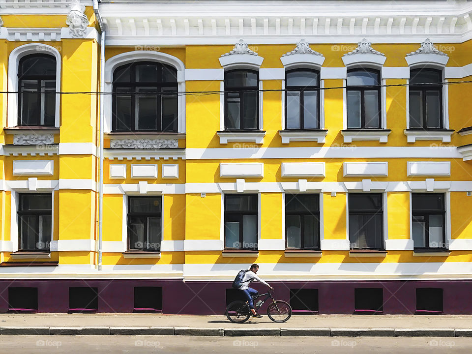 Young man riding a bicycle and using mobile phone in front of the yellow building in the city 