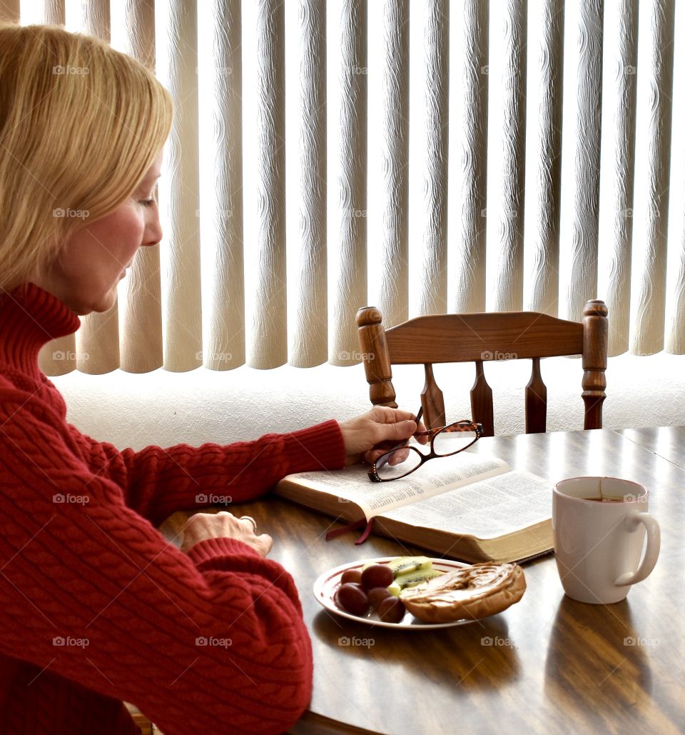 A woman sitting at he breakfast table reading her Bible