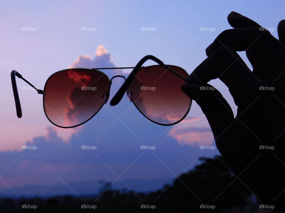 Silhouette and Shadow image - The goggle or sunglasses or Eyewear are hold in hand with sunset background or at blue time.