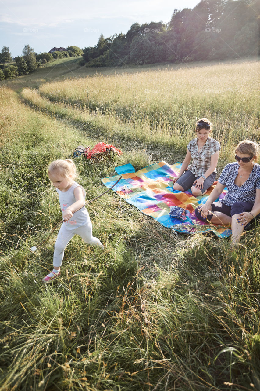 Family spending time together on a meadow, close to nature, roasting marshmallows over a campfire, parents and children playing together and sitting on a blanket on grass. Candid people, real moments, authentic situations