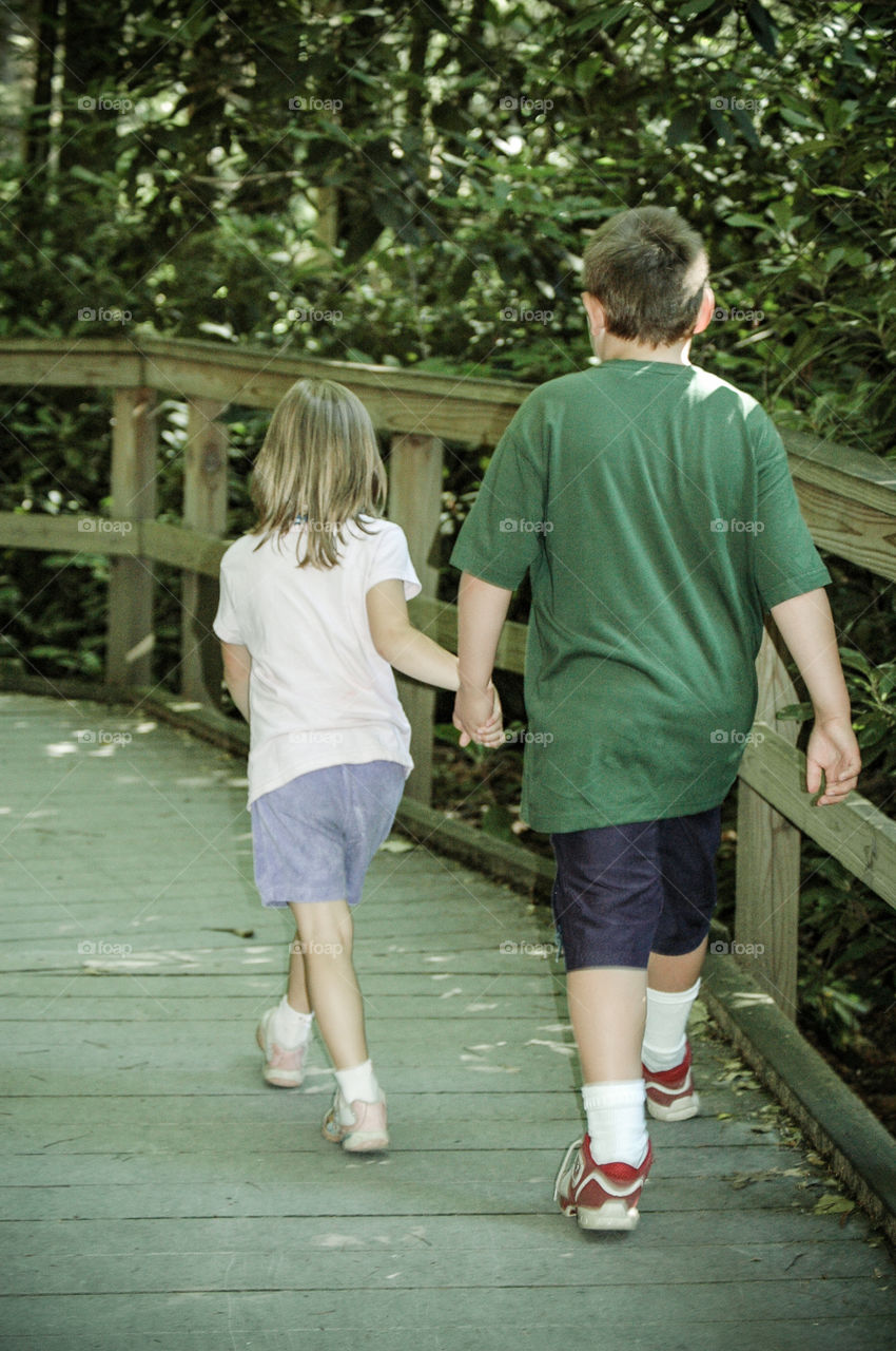 Little girl and bigger boy walking away and hiking path taking a stroll