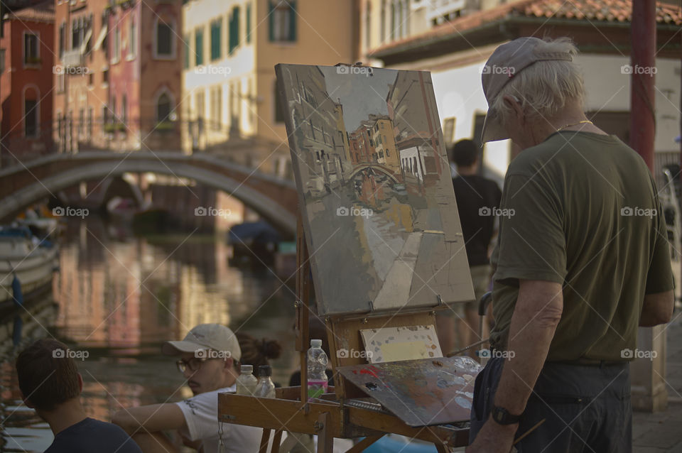 Painter painting a Venice scene live with him the way he is living alive of people and tourists who pass.