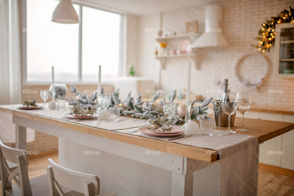 Festive winter cozy kitchen interior with garlands, decorations and gifts.  Christmas dinner at the decorated table.