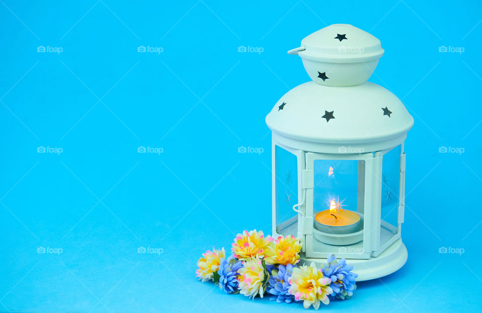 Lanterns with candle light and flowers on blue background with copy space 