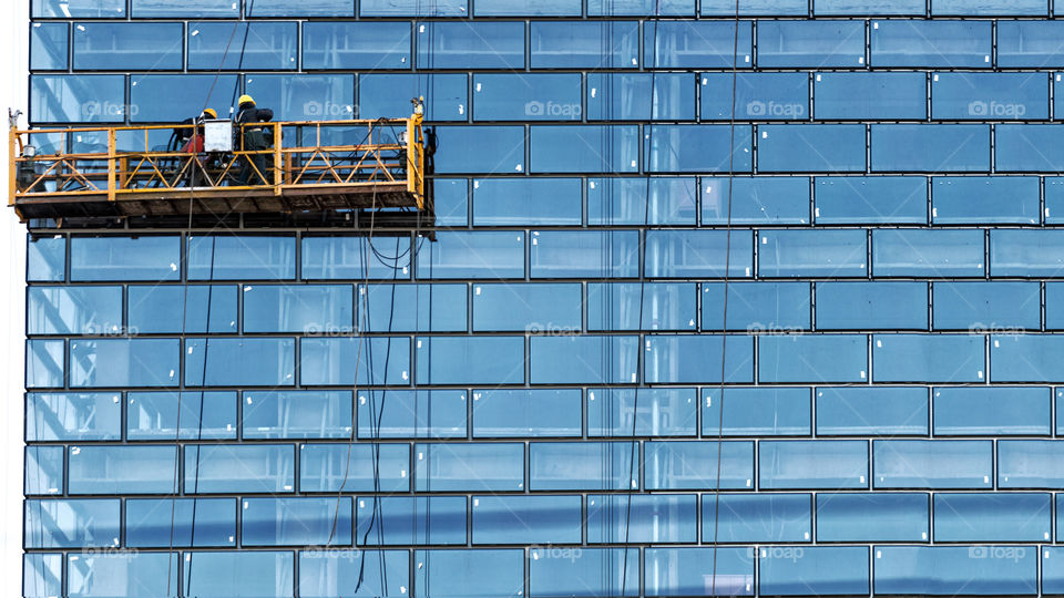 Workers, standing in the ropes installation basket, wash skyscraper windows from the outside.