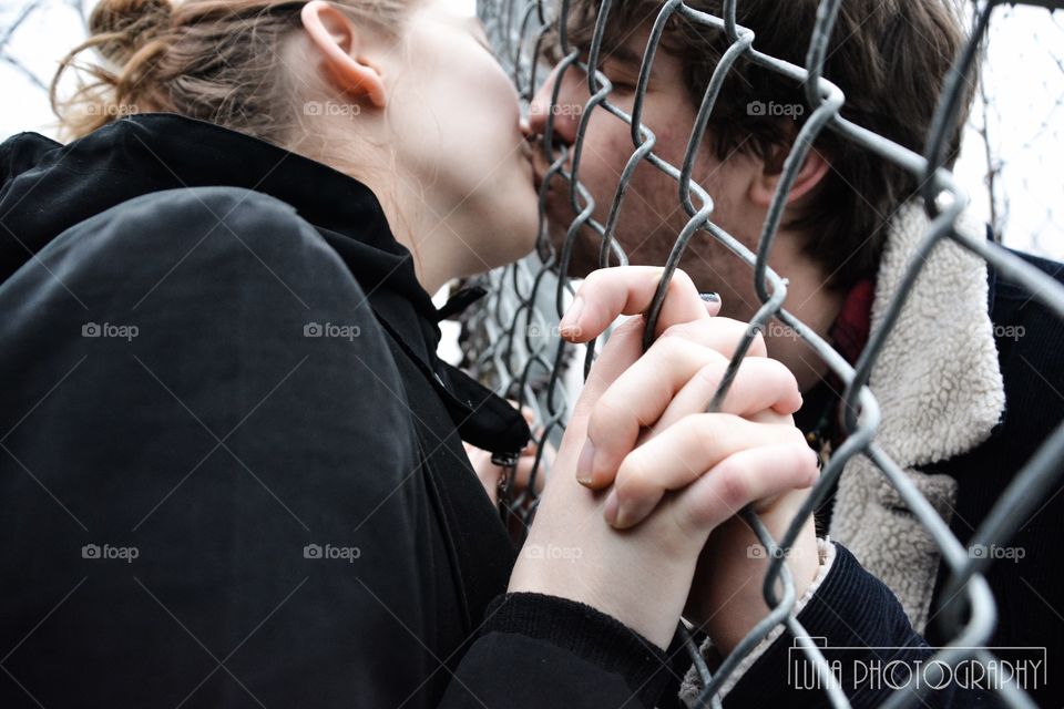 Two lovers kiss separated by a fence 