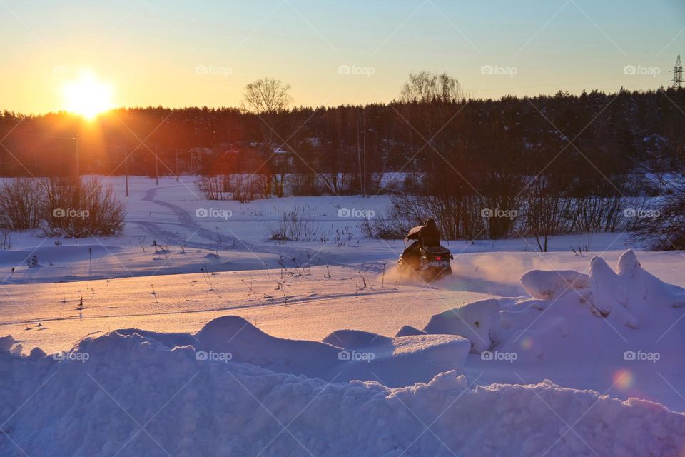 winter evening with setting sun and reflections on the snow man rides a snowmobile